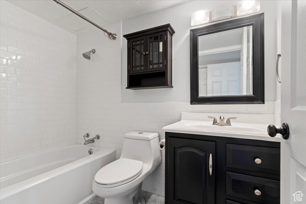 Full bathroom featuring tile walls, toilet, vanity, washtub / shower combination, and wainscoting