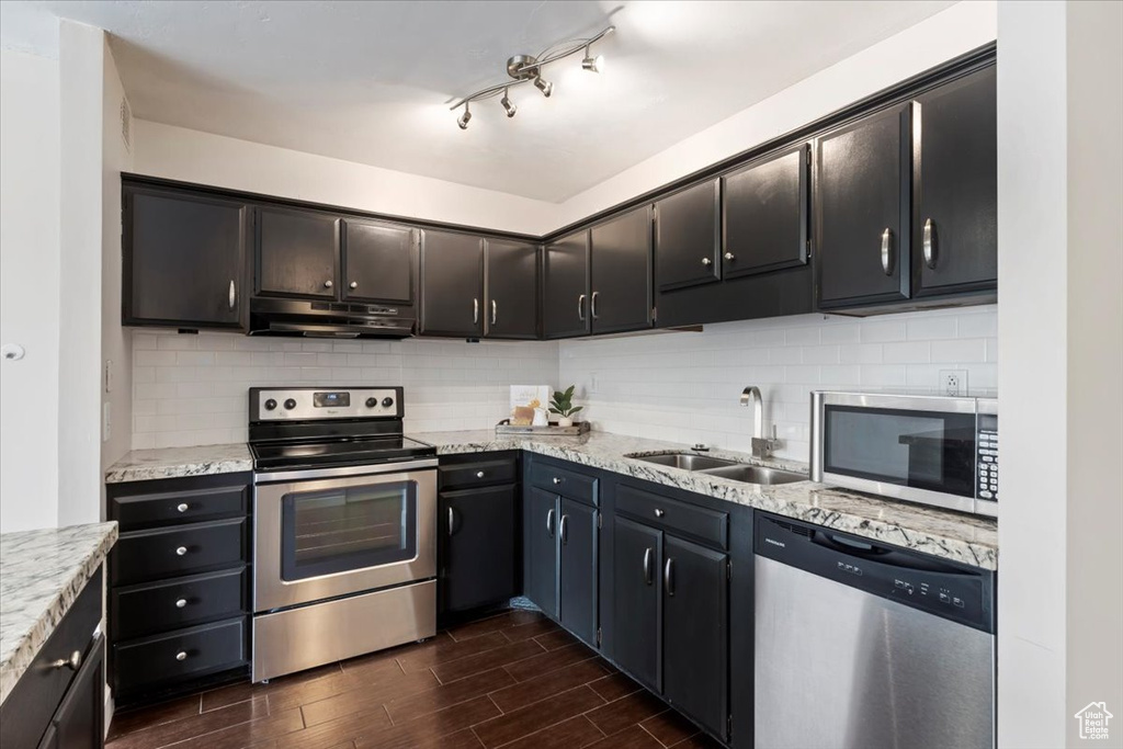 Kitchen with appliances with stainless steel finishes, a sink, dark wood-style floors, under cabinet range hood, and tasteful backsplash