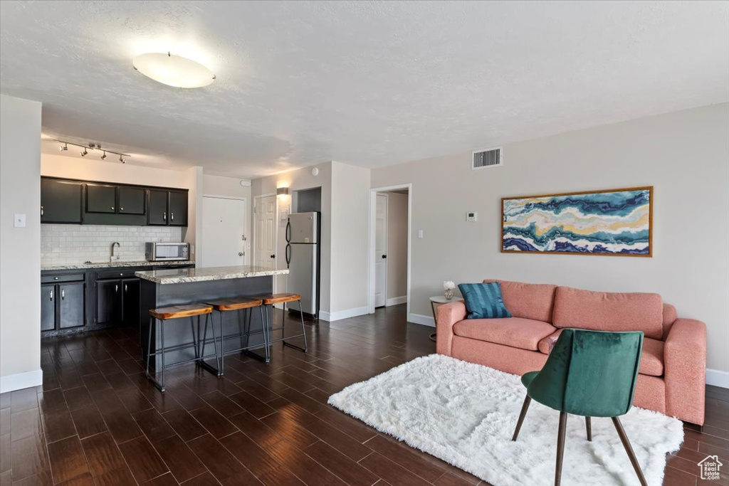 Living area featuring dark wood-style floors, baseboards, and bar with sink