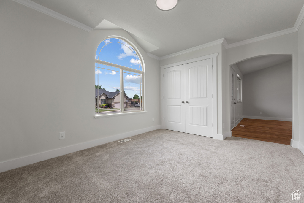 Unfurnished bedroom with arched walkways, vaulted ceiling, carpet, baseboards, and crown molding