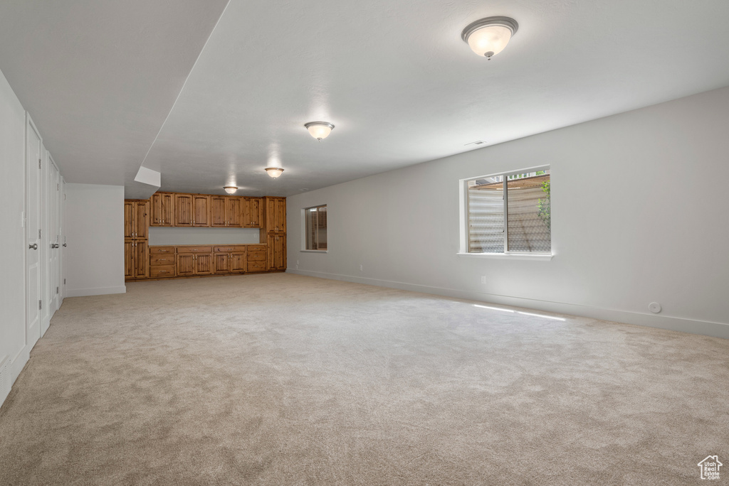 Unfurnished living room featuring light carpet and baseboards