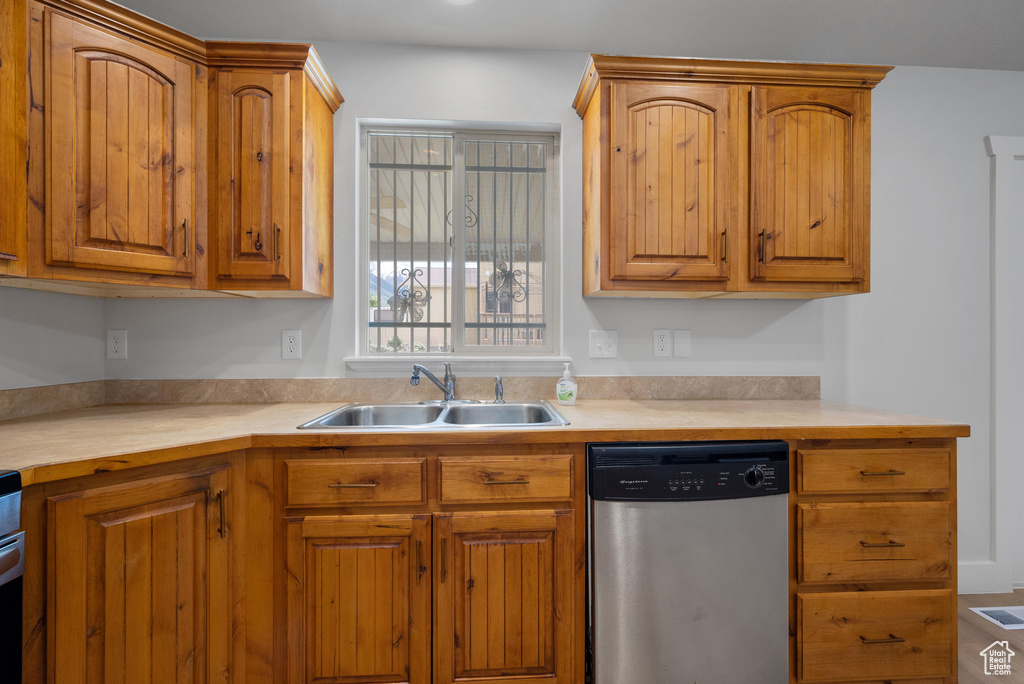 Kitchen featuring stainless steel dishwasher, light countertops, a sink, brown cabinets, and range
