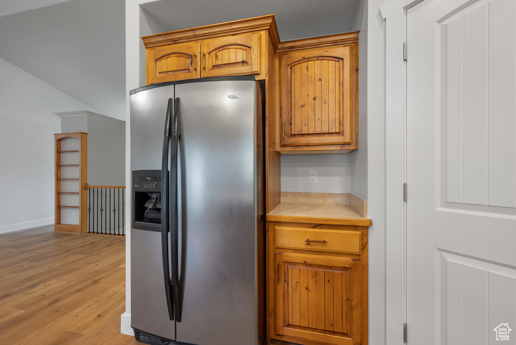 Kitchen featuring stainless steel refrigerator with ice dispenser, light countertops, light wood-style floors, and brown cabinetry
