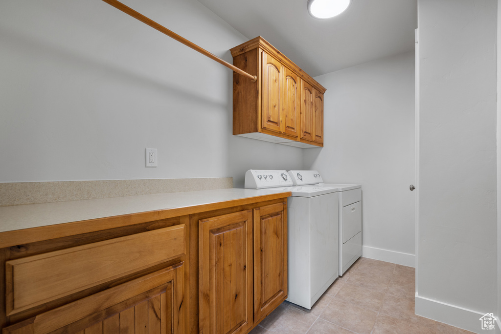 Washroom featuring independent washer and dryer, cabinet space, light tile patterned floors, and baseboards