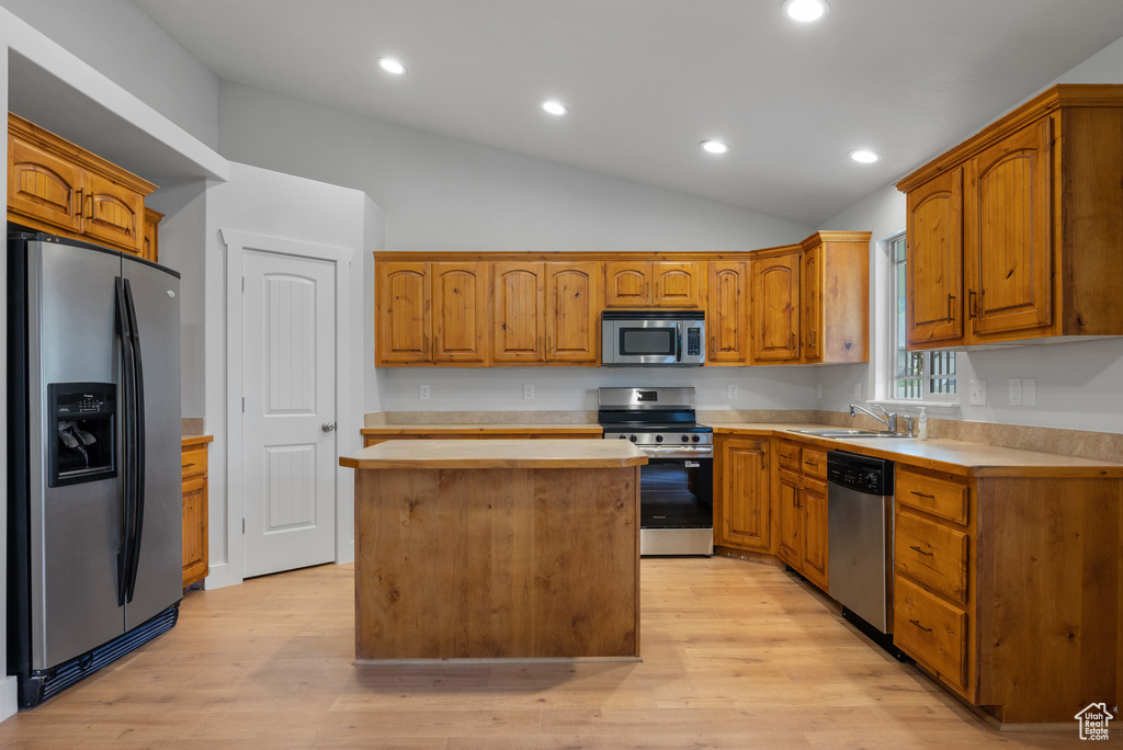 Kitchen with stainless steel appliances, light countertops, a sink, vaulted ceiling, and a center island