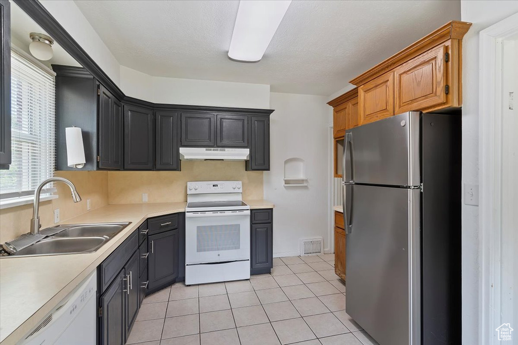 Kitchen featuring white appliances, a sink, under cabinet range hood, light countertops, and light tile patterned flooring