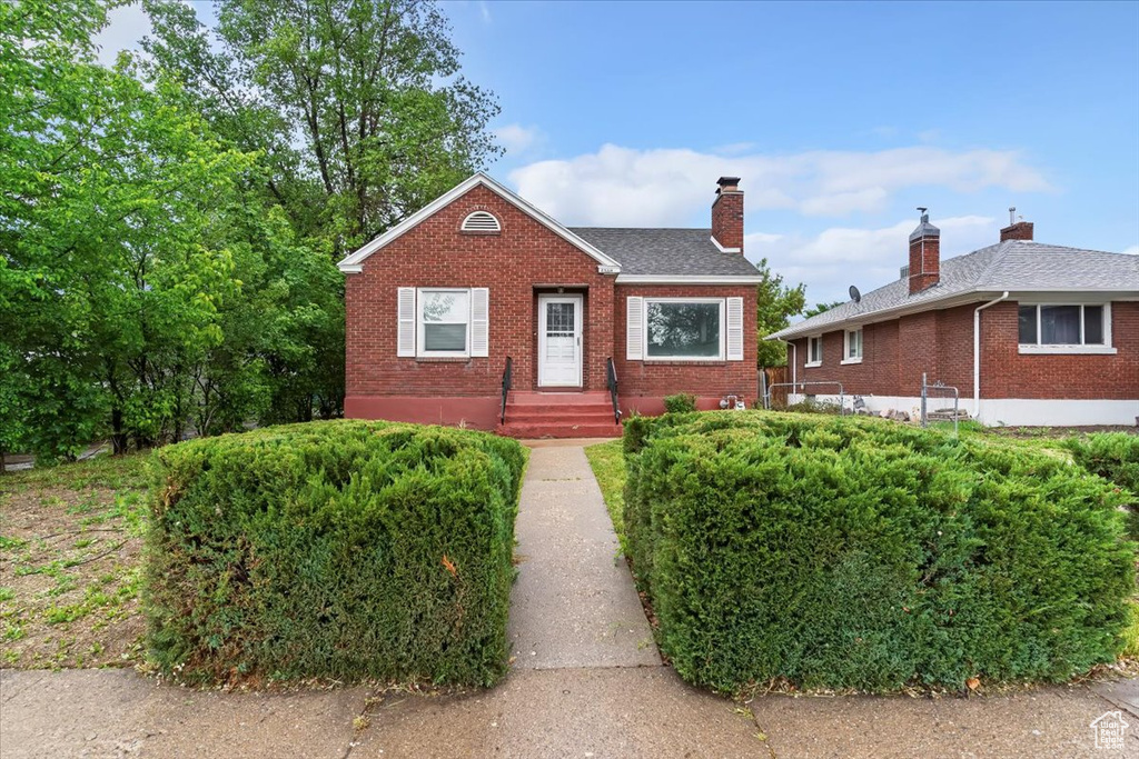 Bungalow-style house featuring brick siding, a chimney, and roof with shingles