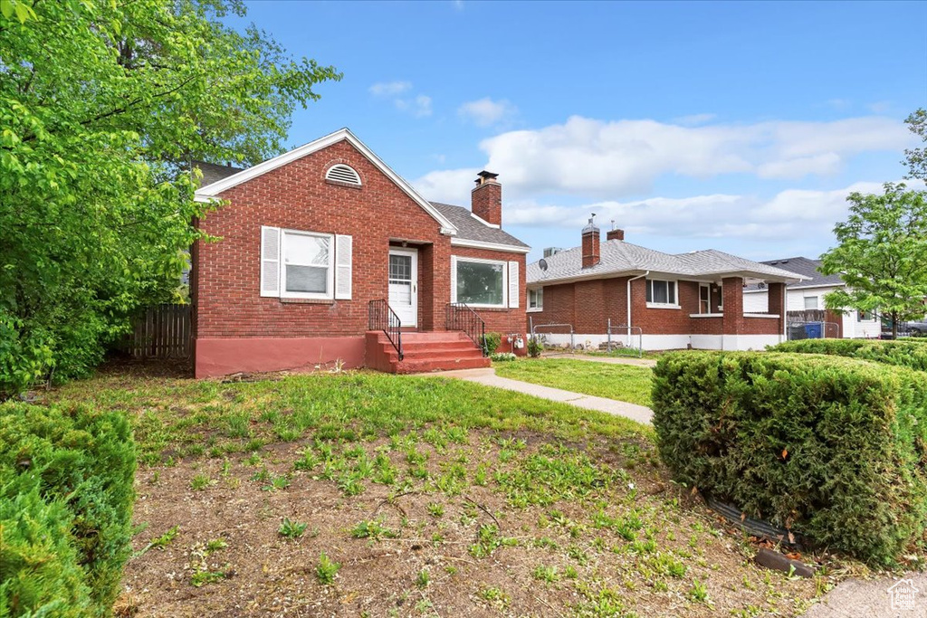 Bungalow-style home with brick siding, a chimney, and fence