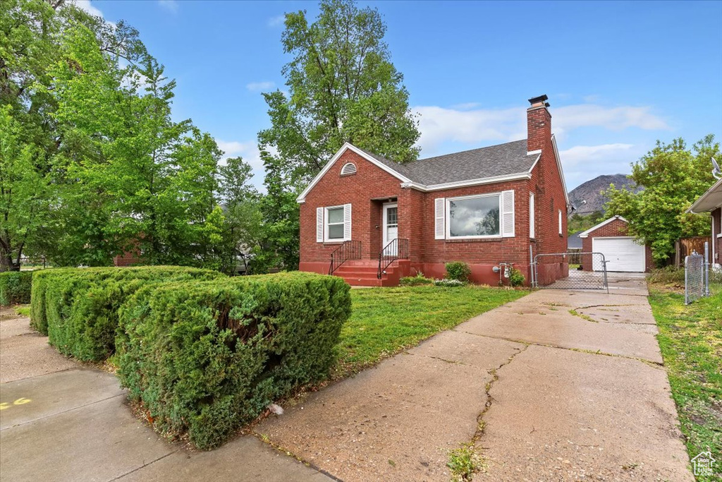 Bungalow-style house with brick siding, a chimney, an outbuilding, roof with shingles, and a detached garage