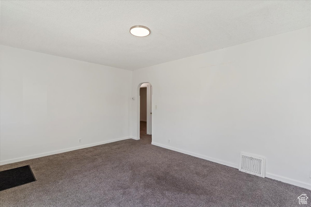 Empty room with arched walkways, dark carpet, and baseboards
