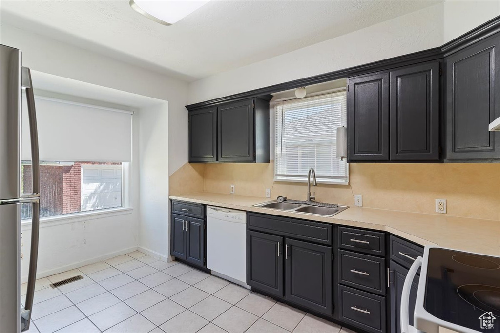 Kitchen featuring a sink, white dishwasher, stainless steel refrigerator, and plenty of natural light