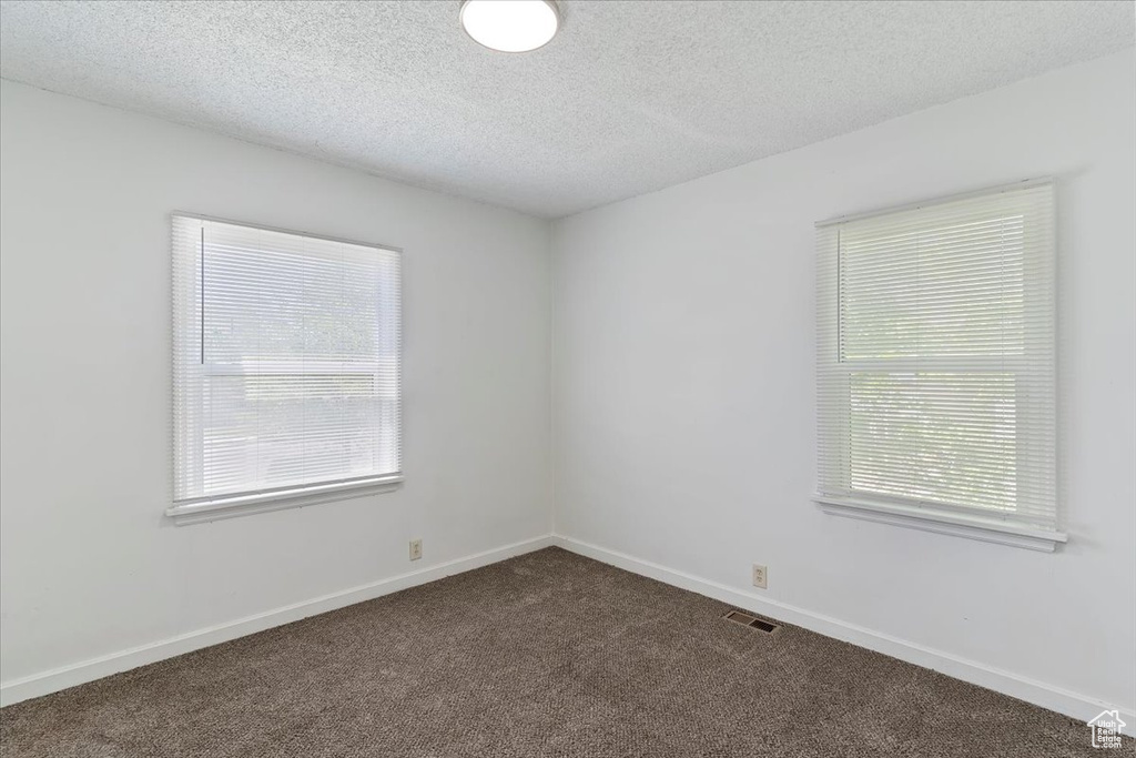 Unfurnished room with dark colored carpet, a textured ceiling, and baseboards