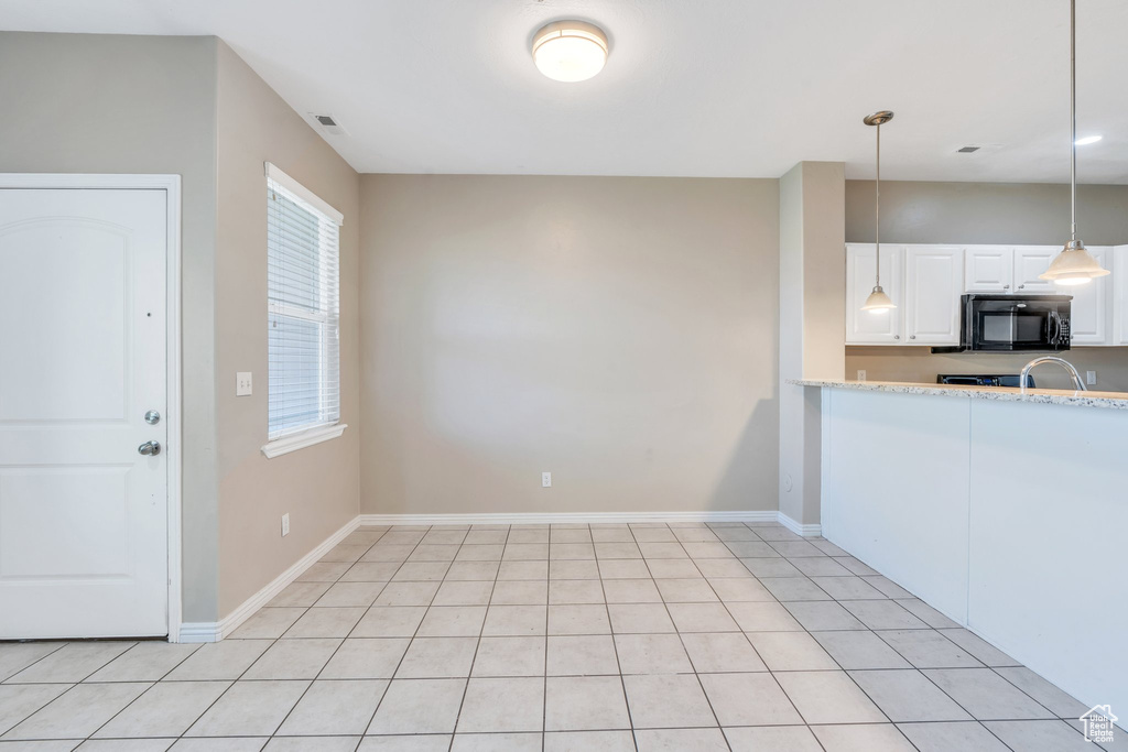Kitchen with black microwave, white cabinets, decorative light fixtures, and baseboards