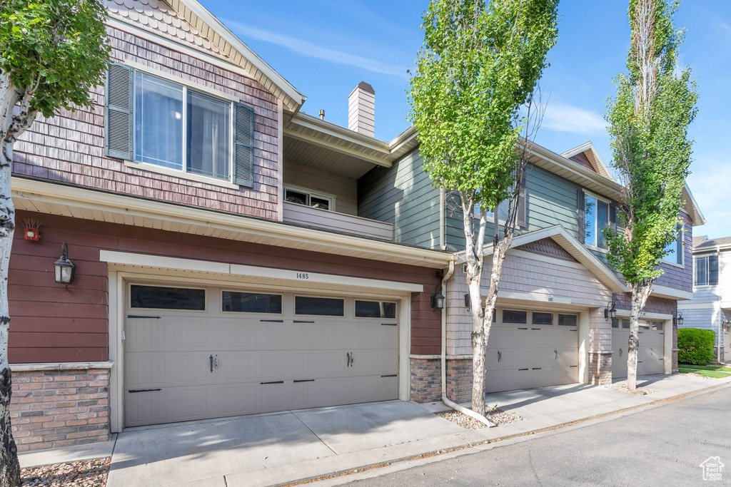 Multi unit property featuring an attached garage, stone siding, and a chimney