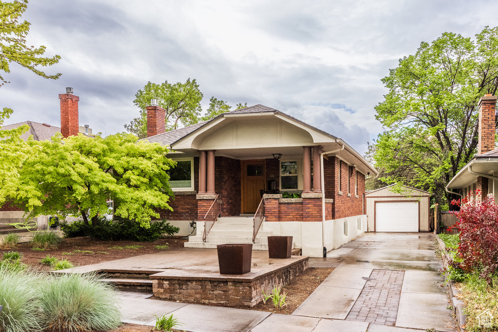 View of front of house featuring brick siding, an outbuilding, a chimney, and a detached garage