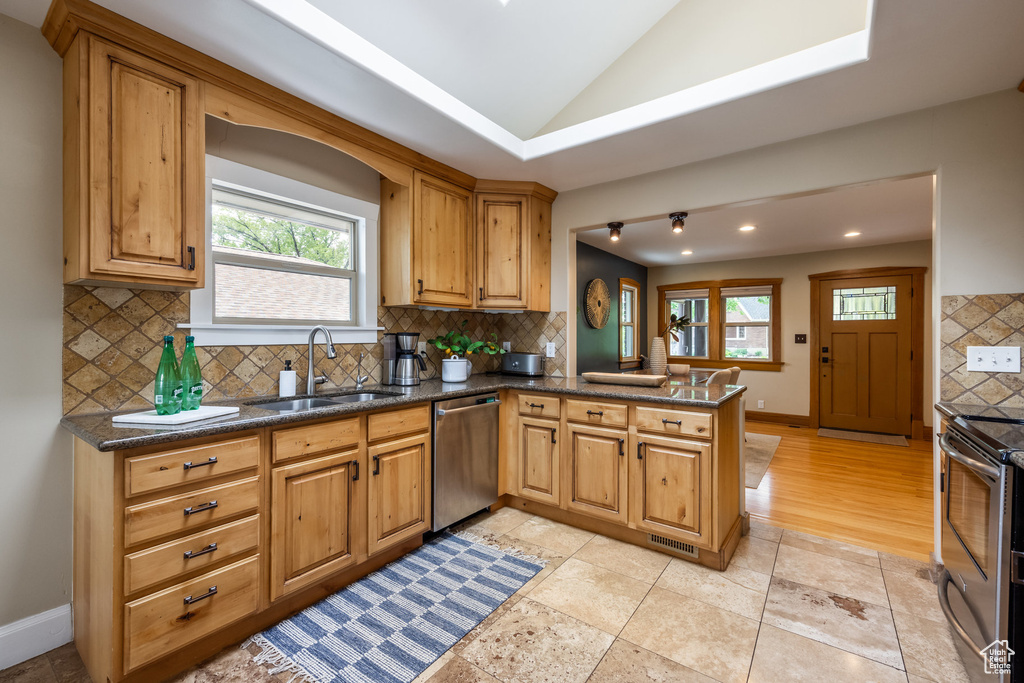 Kitchen featuring stainless steel appliances, a sink, decorative backsplash, a peninsula, and lofted ceiling