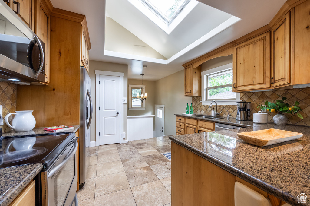 Kitchen with stainless steel appliances, a sink, brown cabinets, a skylight, and vaulted ceiling