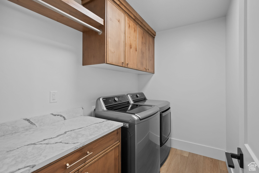 Laundry room featuring cabinet space, separate washer and dryer, light wood-style floors, and baseboards