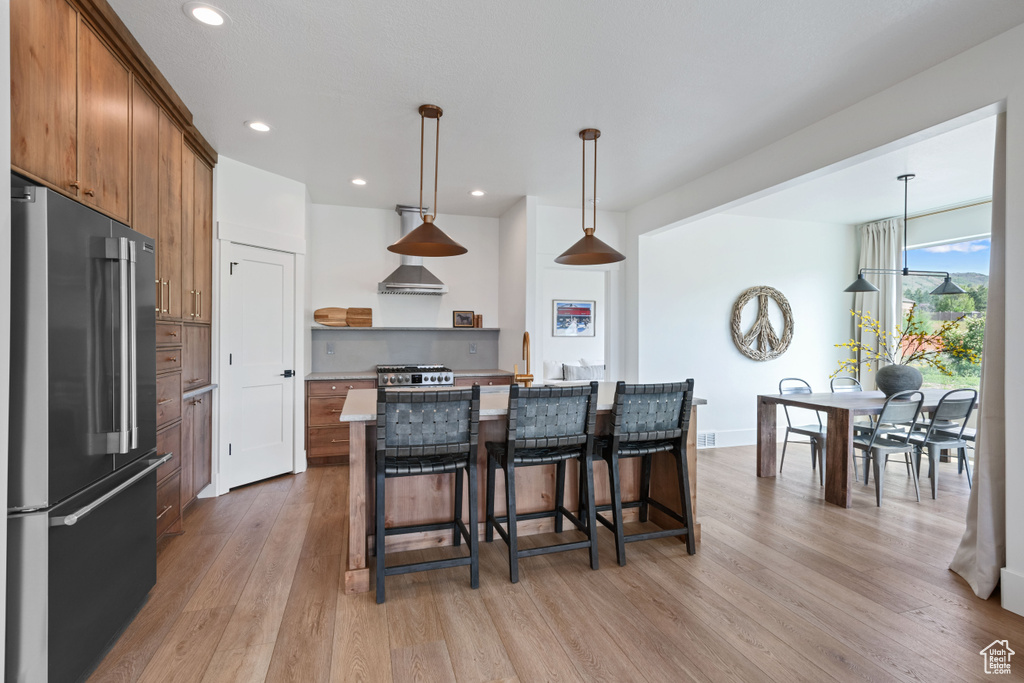 Kitchen featuring high end refrigerator, open shelves, light wood-type flooring, a kitchen bar, and brown cabinetry