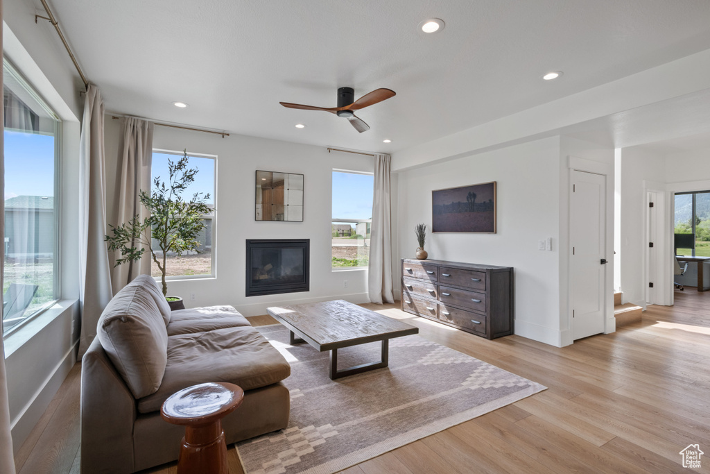 Living room featuring ceiling fan, light wood-style floors, baseboards, a glass covered fireplace, and recessed lighting