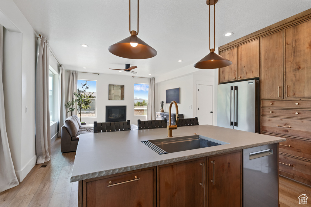 Kitchen with appliances with stainless steel finishes, a sink, open floor plan, a glass covered fireplace, and a center island with sink