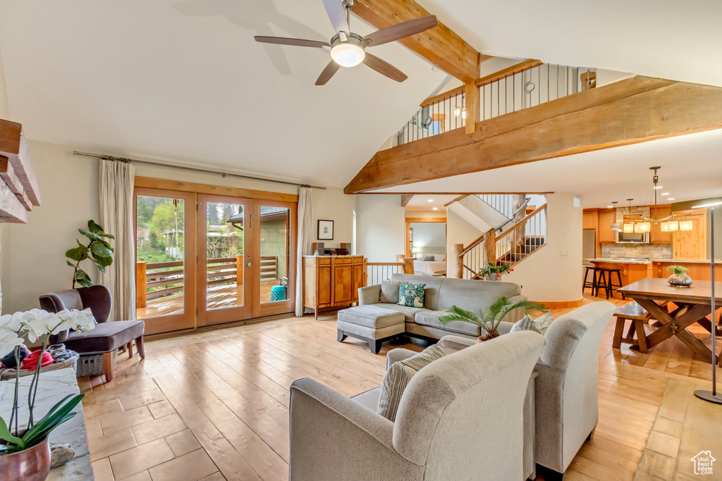 Living room featuring high vaulted ceiling, stairs, light wood-style flooring, ceiling fan, and beam ceiling