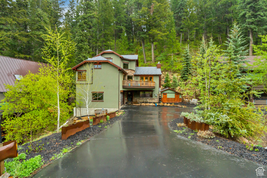 View of front of property with a chimney, a wooded view, asphalt driveway, and metal roof
