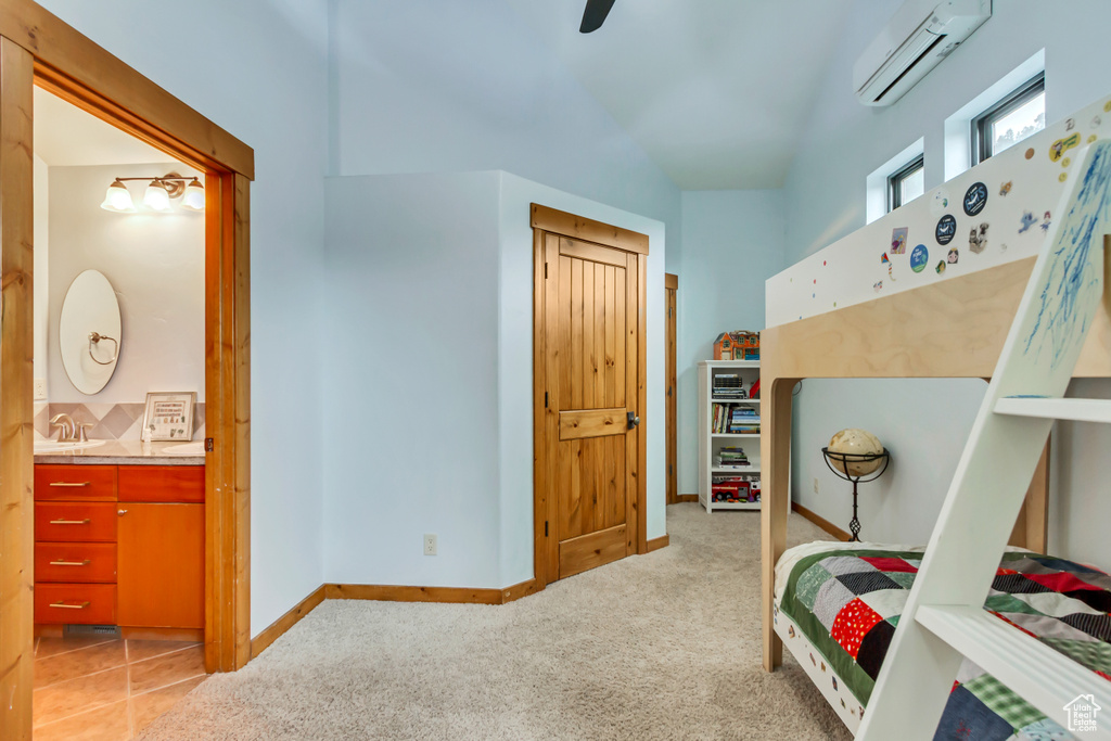 Bedroom featuring a wall mounted air conditioner, light carpet, connected bathroom, baseboards, and a sink