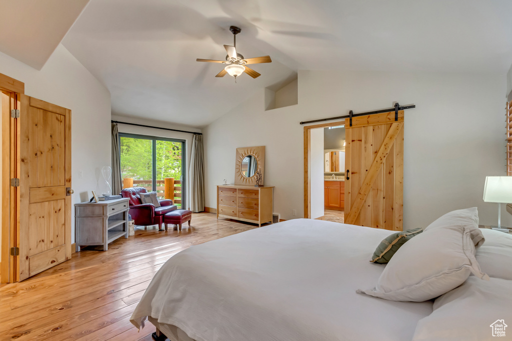 Bedroom featuring a barn door, lofted ceiling, light wood-style flooring, ceiling fan, and connected bathroom