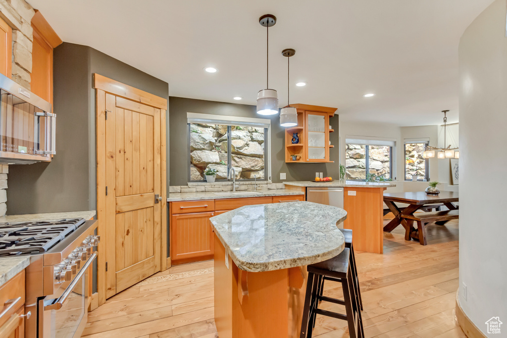 Kitchen featuring appliances with stainless steel finishes, a sink, a kitchen island, light wood finished floors, and light stone countertops