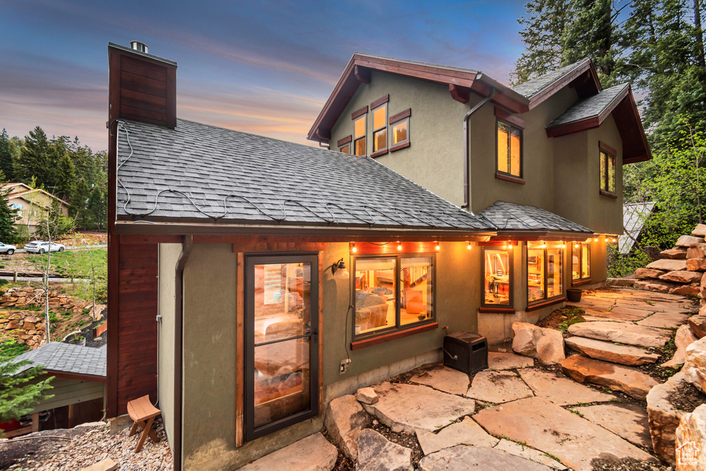 Rear view of property with a shingled roof, a chimney, and a patio