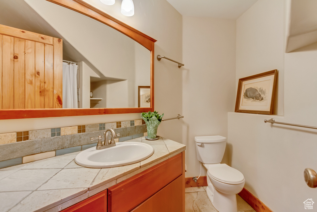 Full bath featuring toilet, vanity, decorative backsplash, and baseboards
