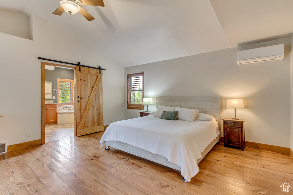 Bedroom with a wall mounted air conditioner, a barn door, light wood finished floors, baseboards, and ensuite bath