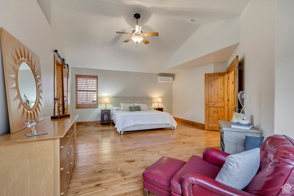 Bedroom featuring a wall mounted AC, a barn door, lofted ceiling, light wood-style floors, and baseboards