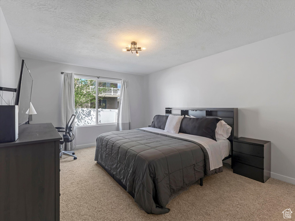 Bedroom featuring light carpet, a textured ceiling, baseboards, and an office area