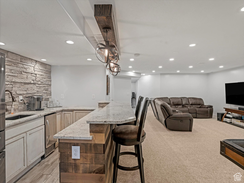 Kitchen featuring a sink, light stone counters, recessed lighting, dishwasher, and a kitchen bar