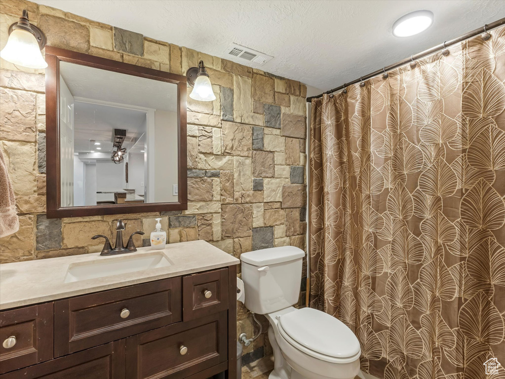 Full bathroom with toilet, vanity, curtained shower, and a textured ceiling
