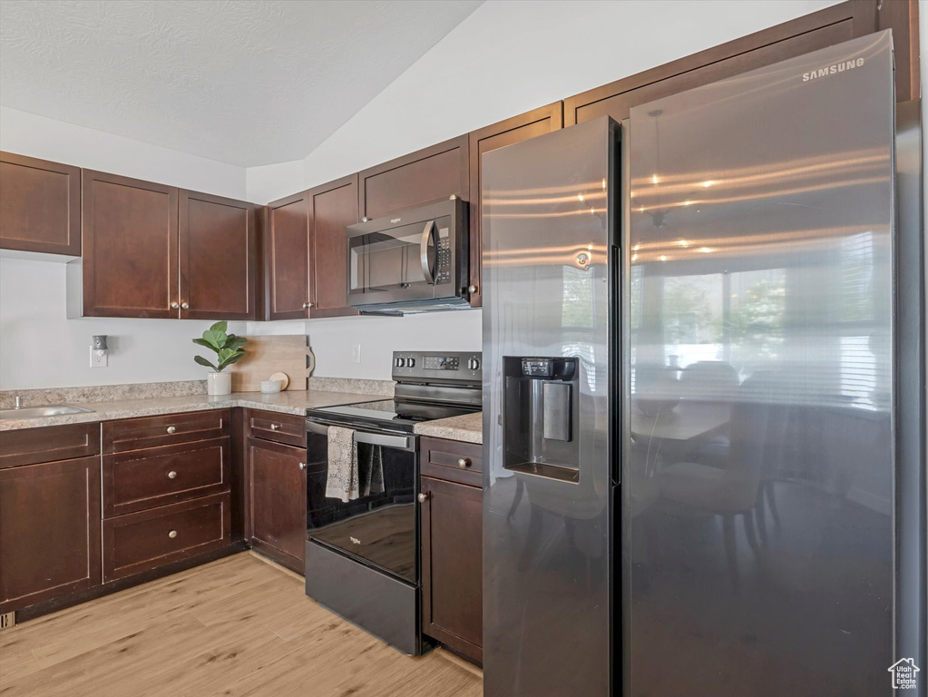Kitchen featuring stainless steel appliances, lofted ceiling, light countertops, light wood-type flooring, and dark brown cabinets