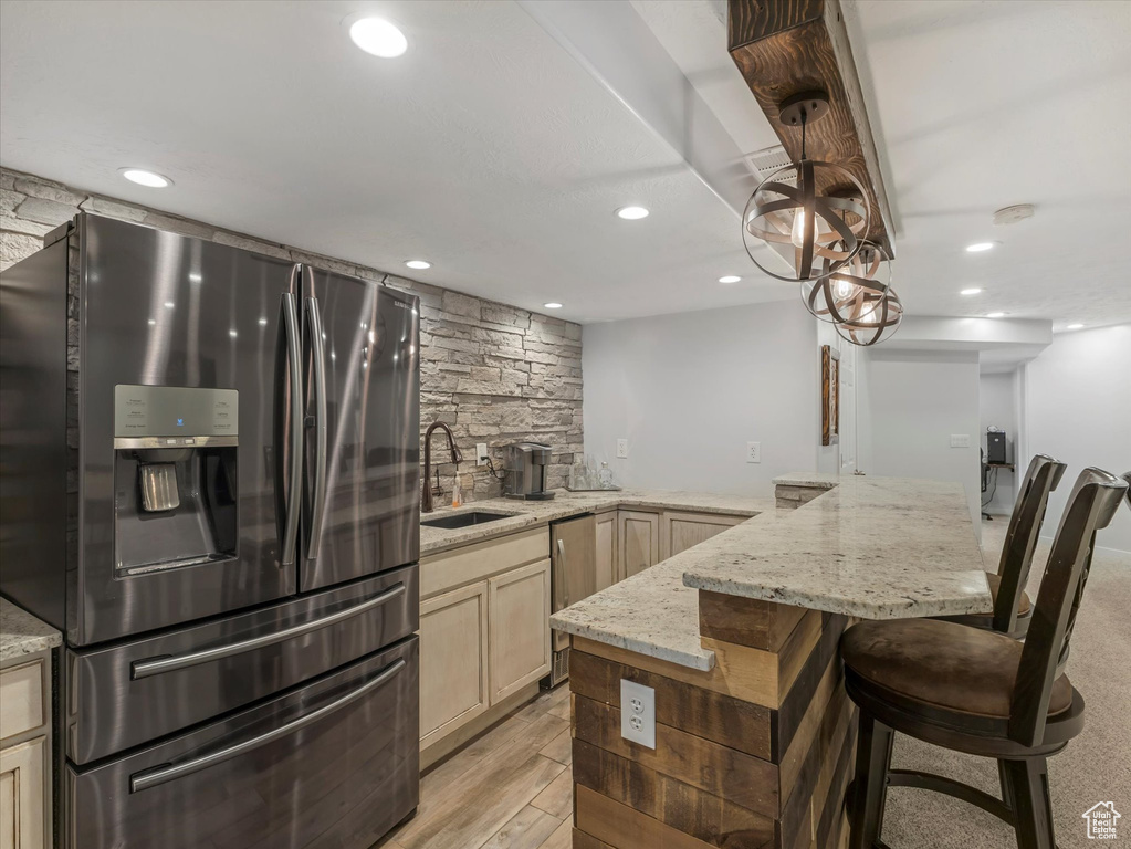 Kitchen featuring stainless steel appliances, a sink, a breakfast bar area, light stone countertops, and recessed lighting