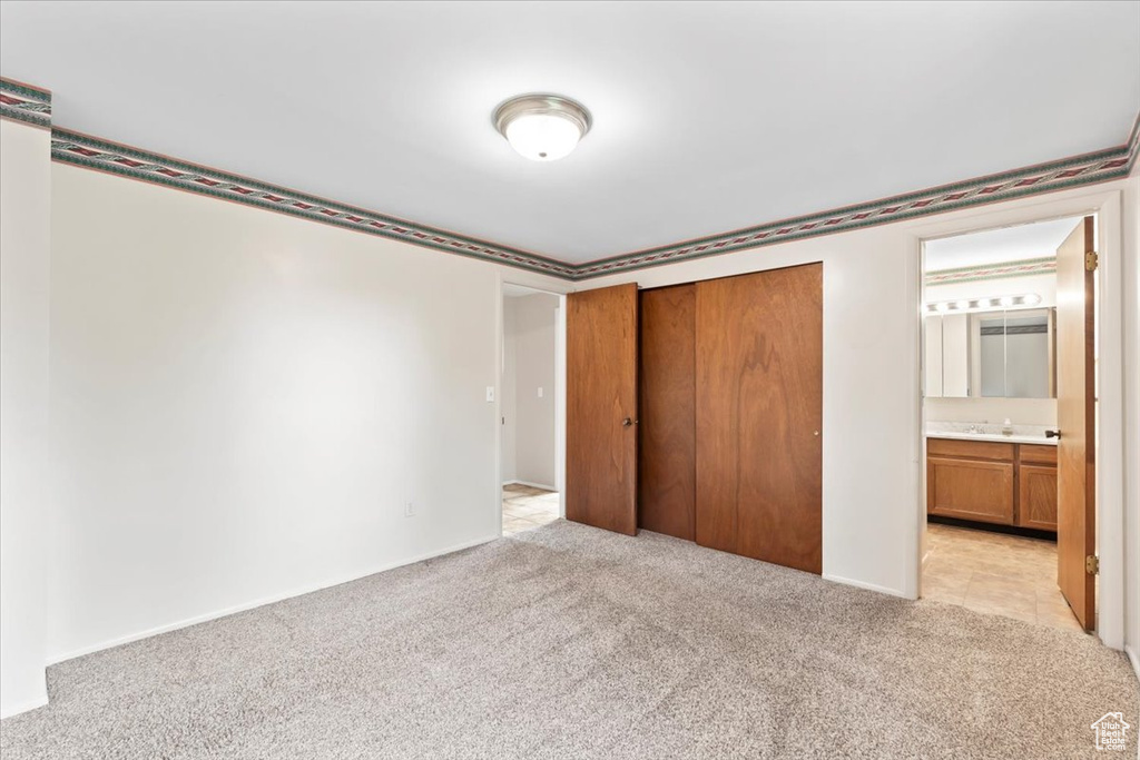 Unfurnished bedroom with light colored carpet, a closet, ensuite bathroom, a sink, and baseboards
