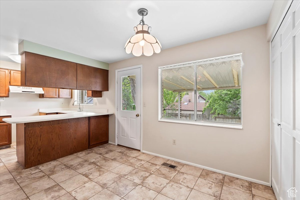 Kitchen with light countertops, baseboards, a sink, under cabinet range hood, and a peninsula
