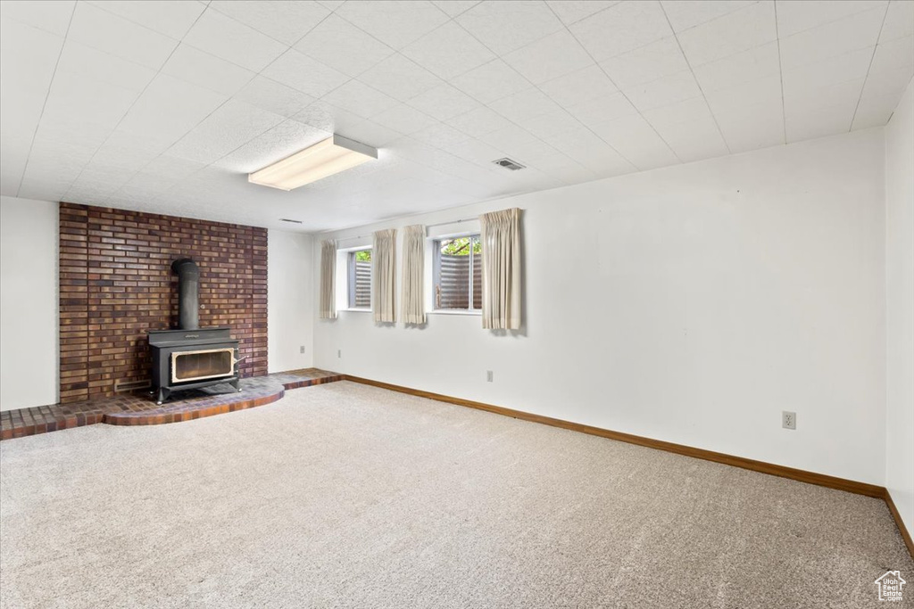 Unfurnished living room featuring a wood stove, carpet flooring, and baseboards