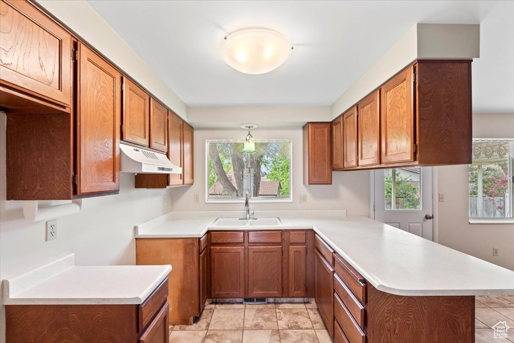 Kitchen featuring under cabinet range hood, a sink, a peninsula, brown cabinets, and healthy amount of natural light
