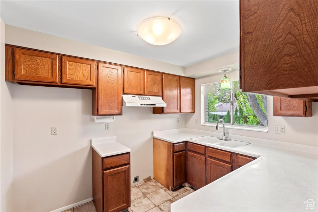 Kitchen featuring a sink, brown cabinets, under cabinet range hood, and light countertops