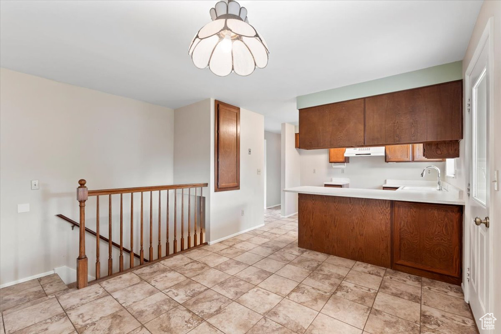 Kitchen featuring range hood, a sink, a peninsula, light countertops, and baseboards