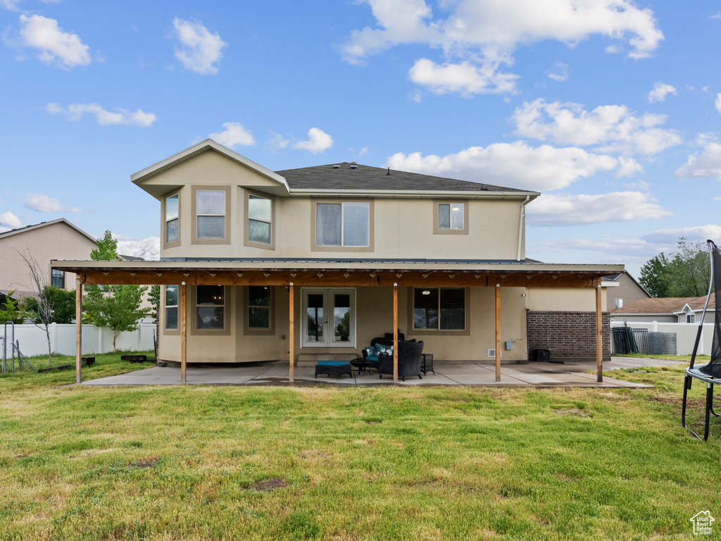Rear view of house with a trampoline, a patio, stucco siding, and french doors