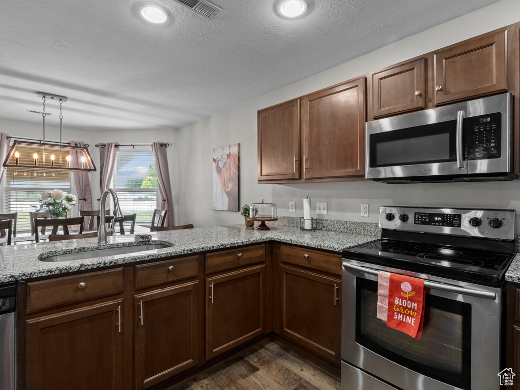 Kitchen with appliances with stainless steel finishes, a sink, dark wood-style flooring, and light stone counters