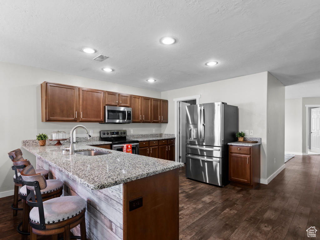 Kitchen featuring appliances with stainless steel finishes, a sink, a peninsula, baseboards, and light stone countertops