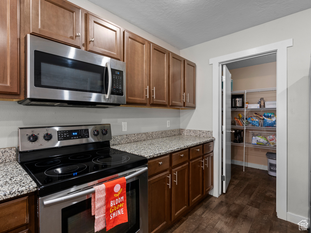 Kitchen featuring appliances with stainless steel finishes, dark wood-type flooring, and light stone countertops