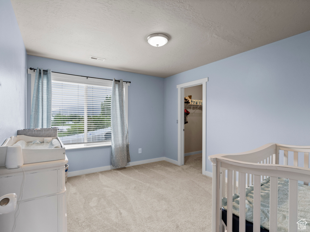 Bedroom with light carpet, baseboards, a textured ceiling, a walk in closet, and a closet